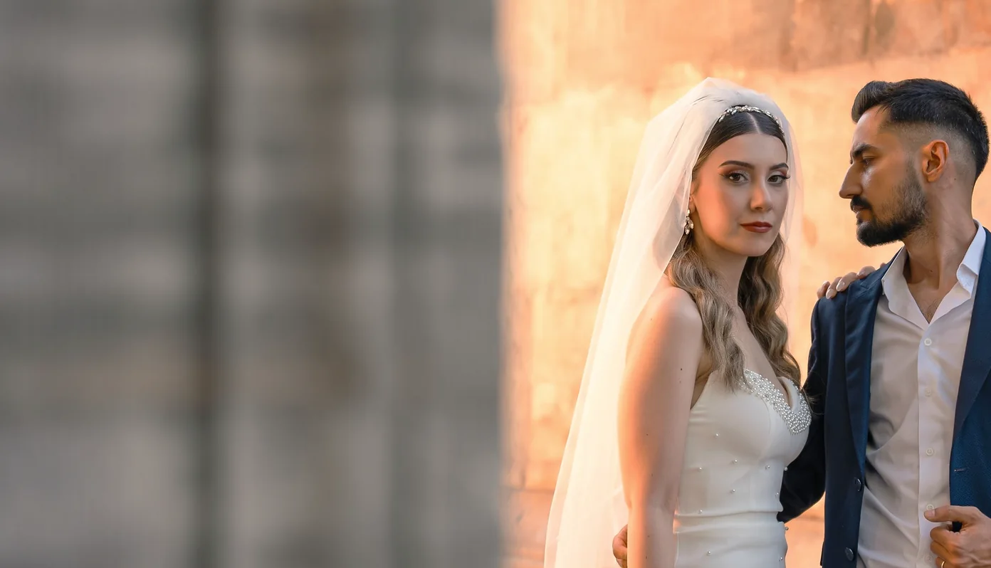 Akşam ışığında taş duvar önünde yan yana duran gelin ve damat
