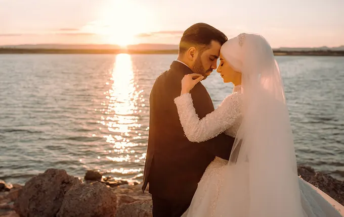 Gün batımında su kenarındaki kayalıklarda sarılan gelin ve damat